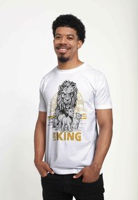 Vit bomull t-shirt med en grafisk av en lejon och ungar, med svarta och gyllene accenter. Designen inkluderar texten "LION KING" framträdande längst ner.