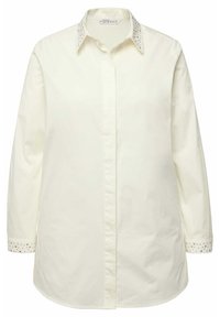 Langærmet skjorte med knapper i lys creme med dekorative nitter på kraven og manchetterne. Lavet af glat stof med en afslappet pasform.