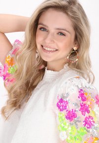 Hvid tekstureret bluse med farverige blomstrede pufærmer i pink, orange og grøn, suppleret med store perlehoop øreringe.
