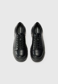 Black leather sneakers with rounded toes, lace-up design, thick rubber soles, and minimalistic accents. Logo visible on the insole.