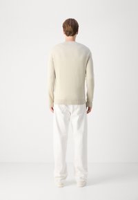 Maglione a maglia beige chiaro con polsini e orlo a costine, abbinato a pantaloni bianchi con vestibilità ampia. Texture liscia e design semplice.