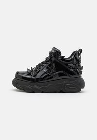 Black patent leather sneakers with a chunky sole, featuring raised butterfly accents, textured fabric panels, and black laces.