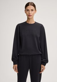 Felpa nera con collo rotondo e maniche lunghe, caratterizzata da testo in rilievo "JOOP! JEANS" sulla parte anteriore. Tessuto morbido, vestibilità comoda.