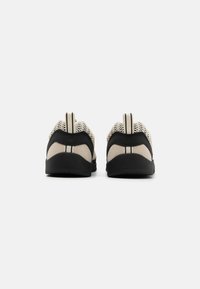 Sneakers z beżową siateczkową cholewą i czarnymi zamszowymi akcentami, z wyściółką w okolicy pięty, pętelką do zakładania oraz teksturowaną gumową podeszwą.