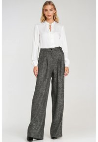 Biała bluzka z długim rękawem i wiązaniem w okolicy szyi oraz czarne, wysokie, szerokie spodnie z fakturowanym wzorem. Całość uzupełniają czarne szpilki.