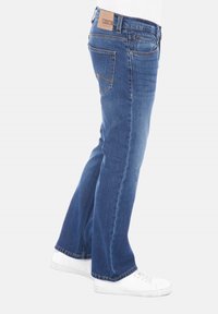 Jeans de mezclilla azul con un diseño de pierna recta, que cuentan con una etiqueta de cuero en la cinturilla y costuras amarillas. Combinados con zapatillas blancas.