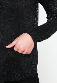 Svart stickad tröja med metalltråd, med långa ärmar och en sidoficka. Ribbad manschett och fåll med en strukturerad finish.