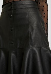 Schwarzer Lederrock mit ausgestellter Silhouette, vorderen Knöpfen und glatter Textur. Das Design umfasst eine V-förmige Naht an der Taille.