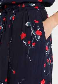 Abito blu navy con motivi floreali rossi e turchesi, con vita con cintura, pieghe e tasche laterali. Tessuto liscio e leggero.