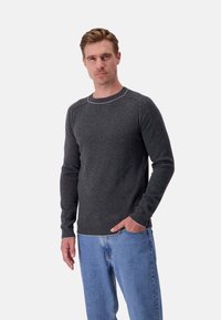 Dunkelgrauer Strickpullover mit Rundhalsausschnitt und subtilen kontrastierenden Nähten. Kombiniert mit hellblauen Jeans. Klassische Passform und glatte Textur.