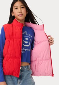 Rode en roze puffer vest met een rits aan de voorkant, voorzien van een geborduurd patroon, zijzakken en een color-block ontwerp, over een blauwe top.