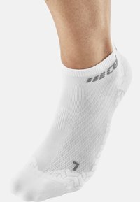 White athletic sock showing a ribbed texture, ankle-height design, and a gray printed number 7 on the side. Zigzag pattern on the cuff.