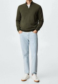 Sweter z zamkiem na szyi w oliwkowym kolorze, jasnoniebieskie dżinsy i białe trampki z brązowymi podeszwami. Prosty design, casualowy krój i miękka tekstura.