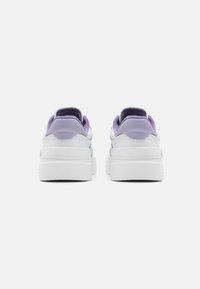White sneakers with a purple heel cap and collar, featuring smooth synthetic material, padded lining, and a thick rubber sole.