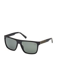 Lunettes de soleil Timberland noires rectangulaires avec des verres foncés et un petit logo sur la branche, inclinées contre un fond blanc.
