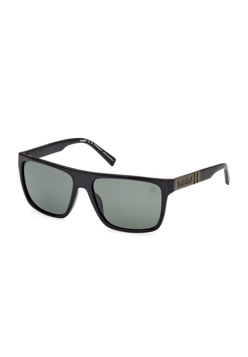 Lunettes de soleil Timberland noires rectangulaires avec des verres foncés et un petit logo sur la branche, inclinées contre un fond blanc.