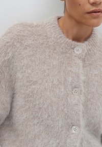Close-up of person wearing a soft, fuzzy light beige cardigan with large buttons and a round neckline.