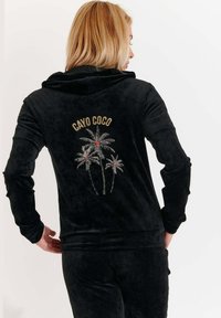 Felpa in velluto nero con la scritta “CAYO COCO” e ricamo di una palma in argento e rosso sulla parte posteriore. Design con cappuccio e maniche lunghe.