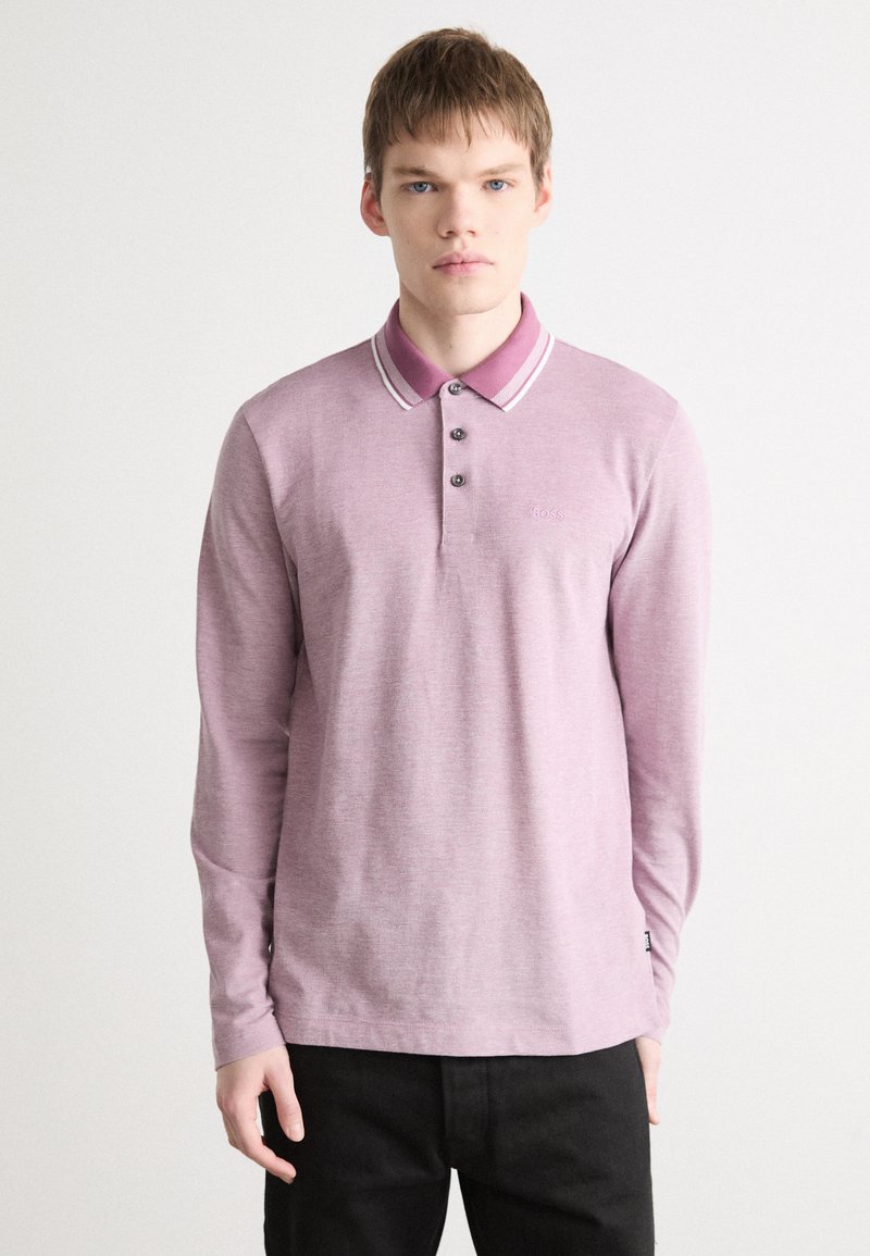 Polo majica s dugim rukavima u svijetlo ružičastoj boji, s kontrastnim ovratnikom sa prugama, pet dugmadi i malim logom na prsima.