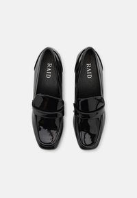 Mocassins en cuir verni noir avec un bout carré et une sangle décorative sur le dessus. L'intérieur présente un logo en blanc.