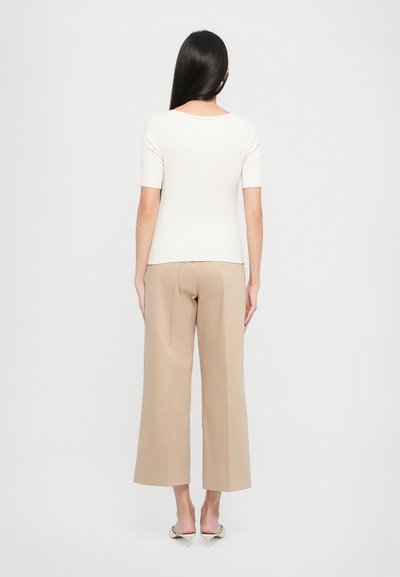 Top bianco a righe con maniche corte e scollo a forma arrotondata sul retro, abbinato a pantaloni larghi beige e sandali con tacco di colore chiaro.