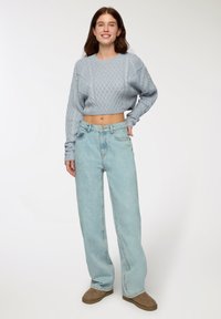 Pullover cropped a maglia blu chiaro con un motivo a rombi, abbinato a jeans in denim chiaro a vita alta. Look casual con tessuti morbidi e strutturati.
