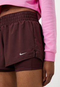 Burgundi futóshort elasztikus derékpánttal, ezüst Nike logóval, rétegzett dizájnnal és oldalvágásokkal a mozgékonyság érdekében.