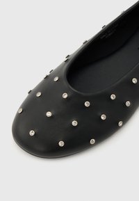 Μαύρο δερμάτινο επίπεδο παπούτσι με στρογγυλή μύτη, διακοσμημένο με ομοιόμορφα τοποθετημένες μικρές ασημί καρφίτσες με καθαρά κρύσταλλα.