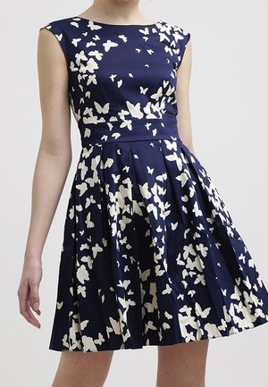 Robe sans manches bleu marine avec corsage ajusté et jupe évasée, présentant des motifs de papillons blancs dispersés sur le tissu.