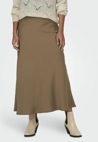 Jupe longue vert olive en tissu lisse, au design évasé. Associée à des bottines crème avec un talon compensé.