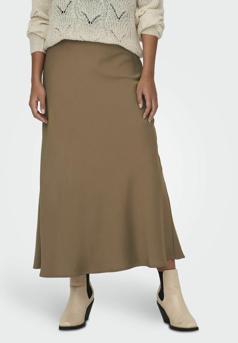 Jupe longue vert olive en tissu lisse, au design évasé. Associée à des bottines crème avec un talon compensé.