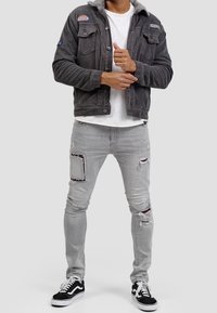 Grijze corduroy jas met een fleece kraag, twee borstzakken en patches. Gecombineerd met lichtgrijze gescheurde spijkerbroek en zwarte sneakers.