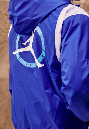 Veste bleue à capuche avec une silhouette blanche d'une personne sautant à l'intérieur d'un cercle bleu clair avec le texte Flight Club dans le dos.