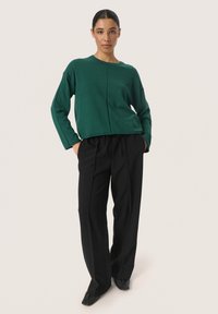 Groene cropped trui met een ronde halslijn en doorvallende schoudernaden, gecombineerd met hoogzitende zwarte broeken met een getailleerde pasvorm.