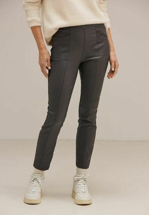 Pantalons en simili cuir noir, avec une coupe slim, présentant des coutures en panneau et une texture lisse. Portés avec des baskets montantes blanches.