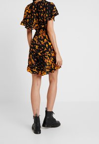 Svart klänning med abstrakt mönster i orange och gult, rynkade ärmar och utsvängd fåll; kombinerad med svarta snörkängor.