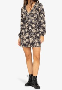 Vestido negro con patrón floral, de manga larga, escote en V y cintura fruncida. Combinado con botas negras de cordones hasta el tobillo.
