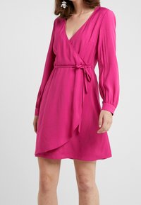 Fuksjowa sukienka kopertowa z długimi rękawami, dekoltem w kształcie litery V, przewiązywanym paskiem po boku i rozkloszowanym dołem. Gładki materiał o subtelnym blasku.