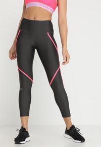 Leggings noirs avec des accents diagonaux roses, taille haute, fabriqués en matériau extensible, assortis à des chaussures de sport noires.