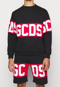 Completo di felpa nera e pantaloni corti, caratterizzato da audaci strisce in rosso e bianco con logo. Il materiale sembra morbido; il design è sportivo con una vestibilità comoda.
