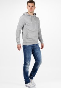 Sweatshirt à capuche gris avec une poche kangourou, associé à un jean bleu délavé et des baskets blanches. Design simple et coupe décontractée.