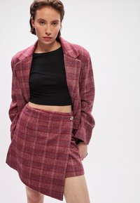 Karo jaka un apļa svārki bordo un rozā toņos, tekstūrēts audums, ar ziedu akcentu uz svārku sāna. Melns cropped tops zem tā.