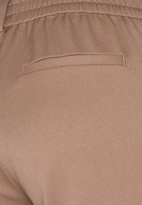 Beige, texturovaná tkanina má jemnou strukturu a zadní kapsu. Pas je elastický pro pohodlí a flexibilitu.