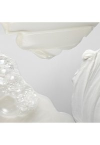 Tre creme cosmetiche bianche con diverse texture, tra cui liscia, montata e spumosa, su uno sfondo grigio chiaro.