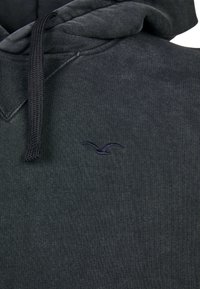 Dark gray hoodie made of soft fabric, featuring a kangaroo pocket and a small purple bird logo on the left chest area.
