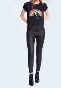 Sort cropped t-shirt med et regnbuefarvet grafisk motiv og et lyn, kombineret med tætsiddende sorte læderbukser og sorte ankelstøvler.