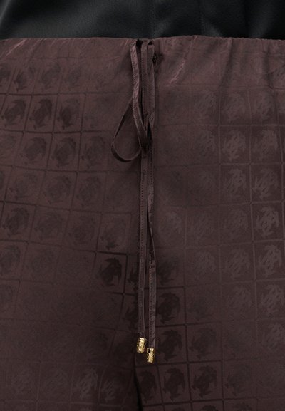 Σκούρο καφέ ύφασμα με διακριτικό σχέδιο πλέγματος και λουλουδάτες λεπτομέρειες, με δύο κρεμασμένα κορδόνια σύσφιξης με μεταλλικές άκρες σε χρυσό χρώμα.