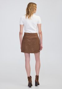 Mini falda marrón texturizada con una cinturilla alta, dos bolsillos traseros y una ligera forma en A, combinada con una blusa blanca de manga corta.