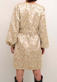 Kort sidentklänning med ett guld abstrakt mönster, elastisk midja, puffärmar och rundad halsringning, med en slät, glansig textur.