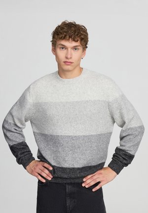 Maglioncino a righe grigio e bianco, con colletto rotondo, polsini e orlo a costine. Presenta una sfumatura dal grigio chiaro al grigio scuro.